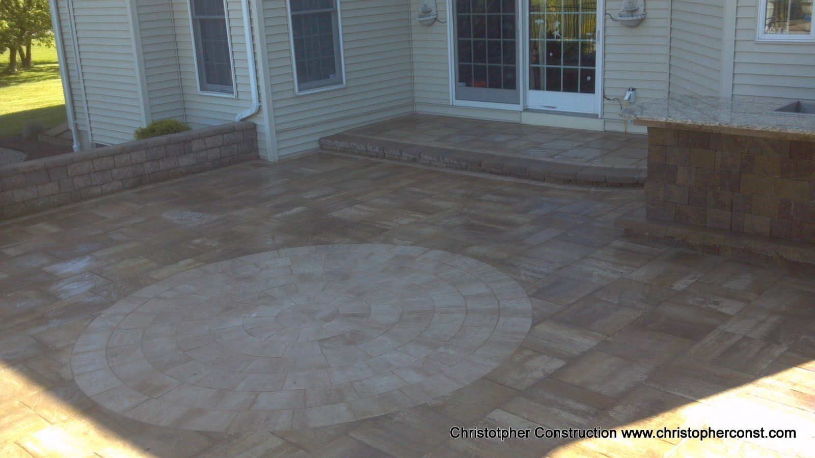 Stone patio with circular inlay in front of sliding glass doors on a house exterior