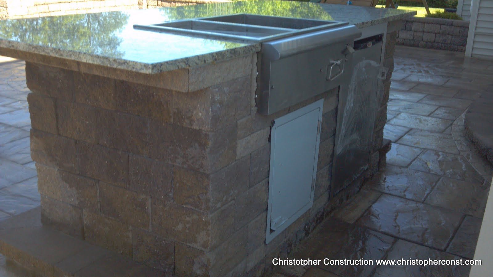 Stone outdoor grill island with a metal lid and cabinet door on a patio