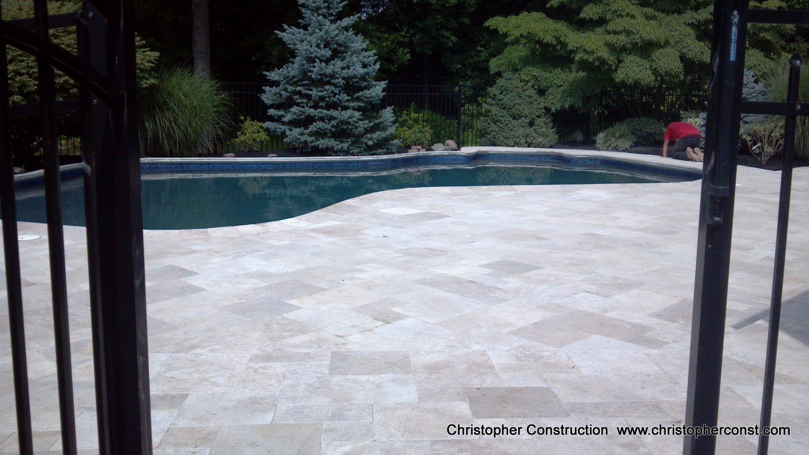 Stone patio beside a backyard swimming pool, framed by dark metal gate posts.