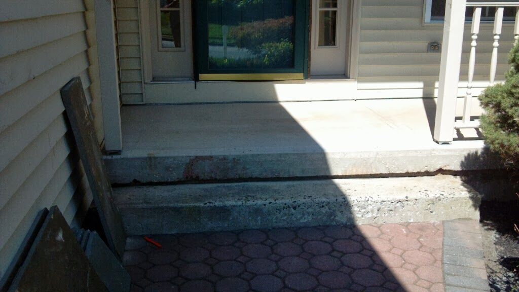 Front porch with concrete steps, a glass door, and sunlight casting a shadow across the entrance.