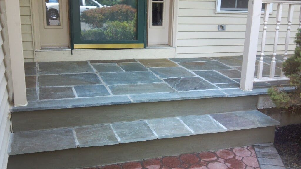 Front porch with tiled steps, white siding, and a glass front door.