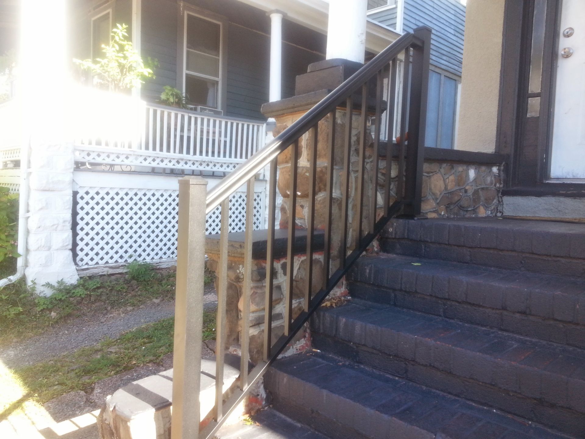 Front porch stairs with black railing beside a white house and lattice skirting