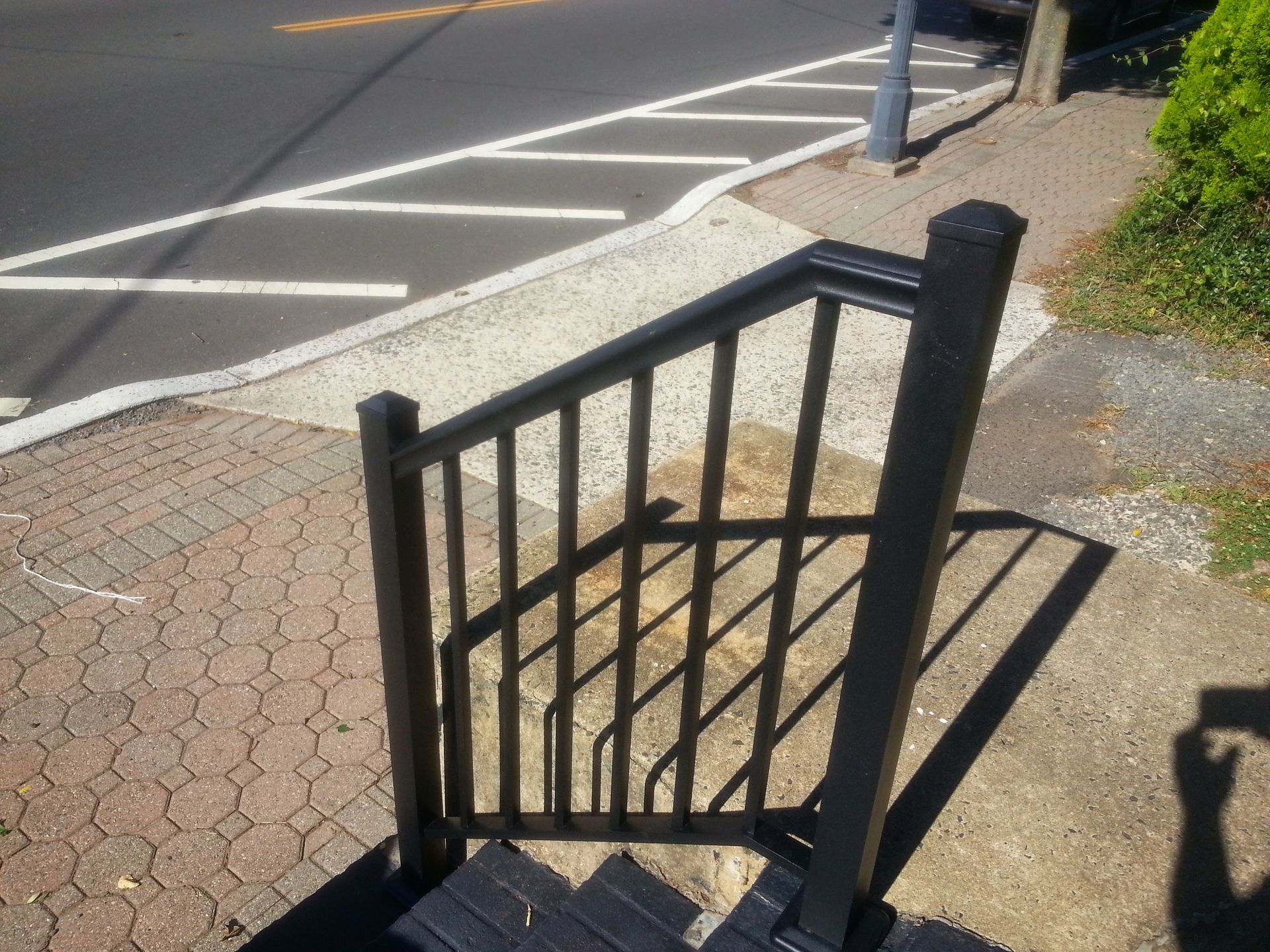 Black metal railing beside a sidewalk ramp and curb at a street corner