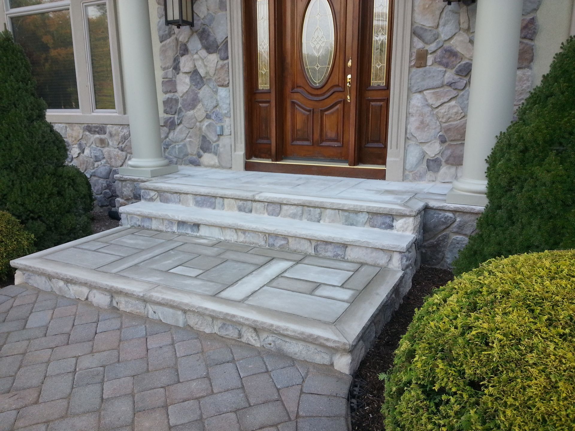 Front entrance with steps and a wheelchair ramp leading to a wooden door, bordered by stone and shrubs