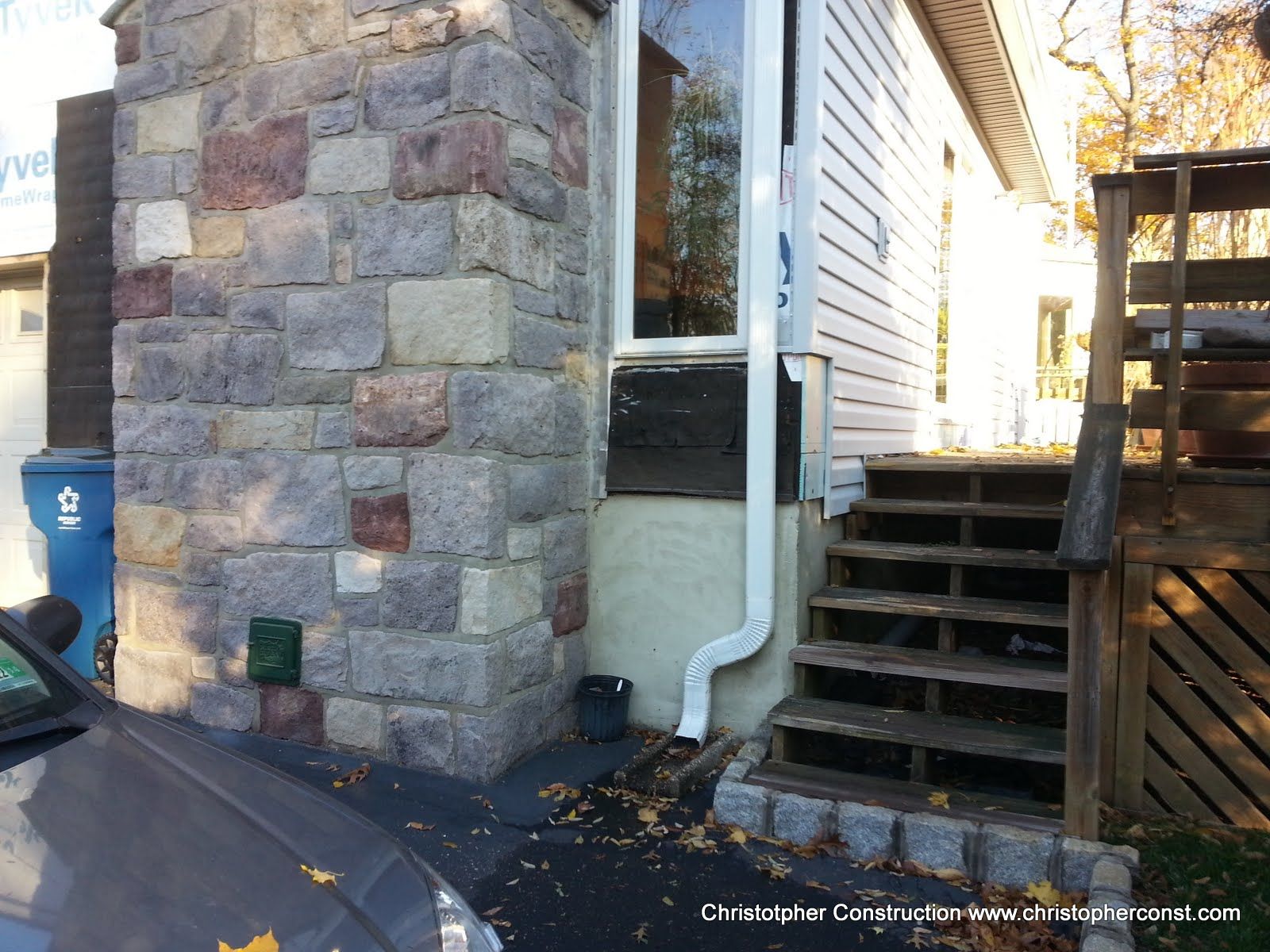 Stone house corner with white siding, outdoor stairs, and a blue mailbox beside a driveway