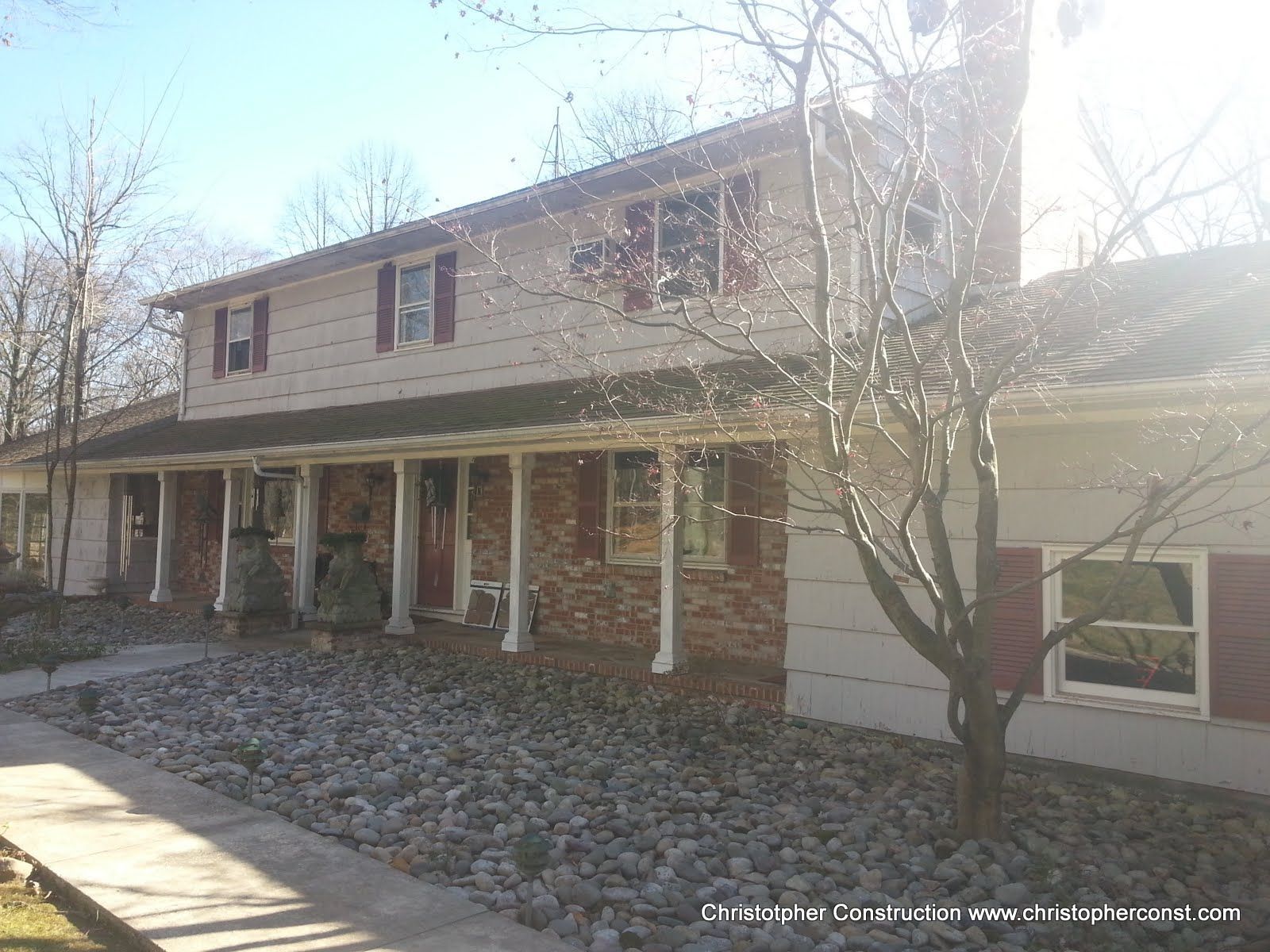 Two-story house with a front porch, brick lower level, and attached garage in winter sunlight