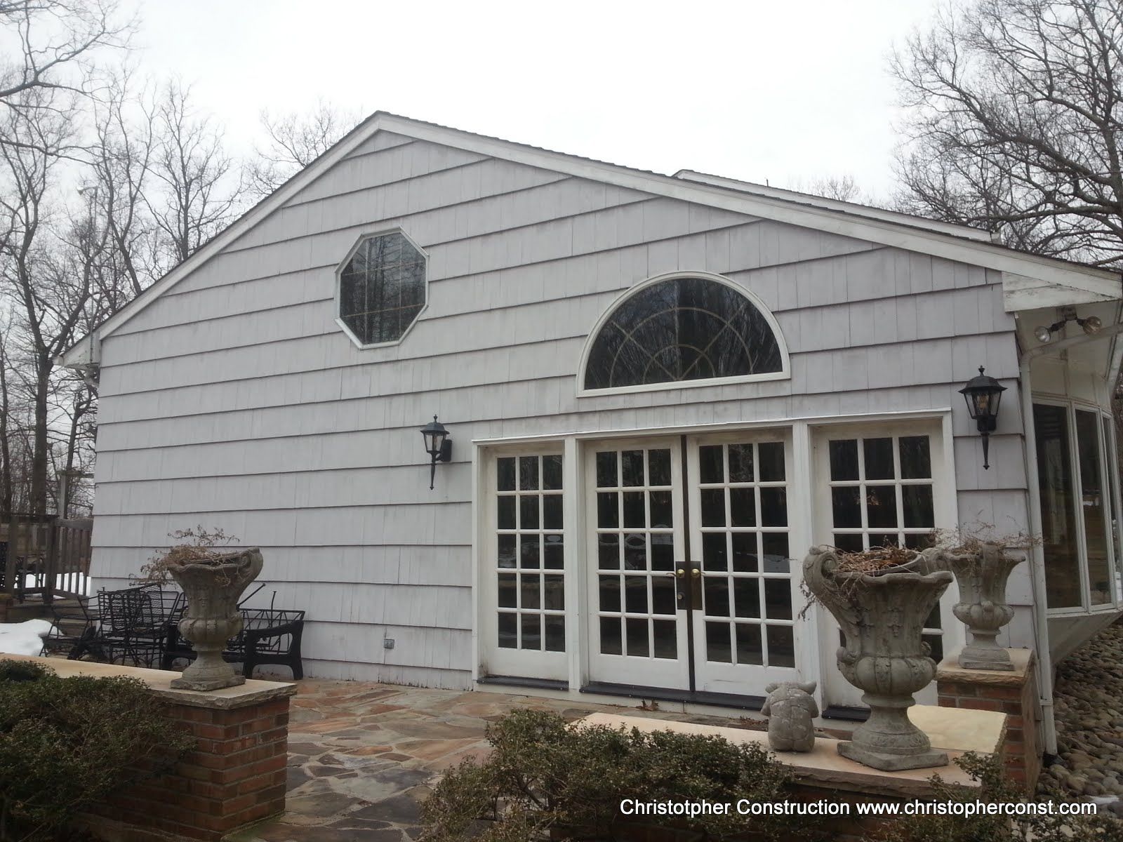 White house with arched windows, French doors, and brick planters on a stone patio.