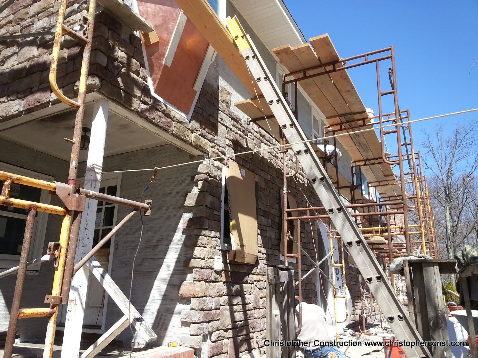Scaffolding and construction work beside a stone building wall under a clear blue sky