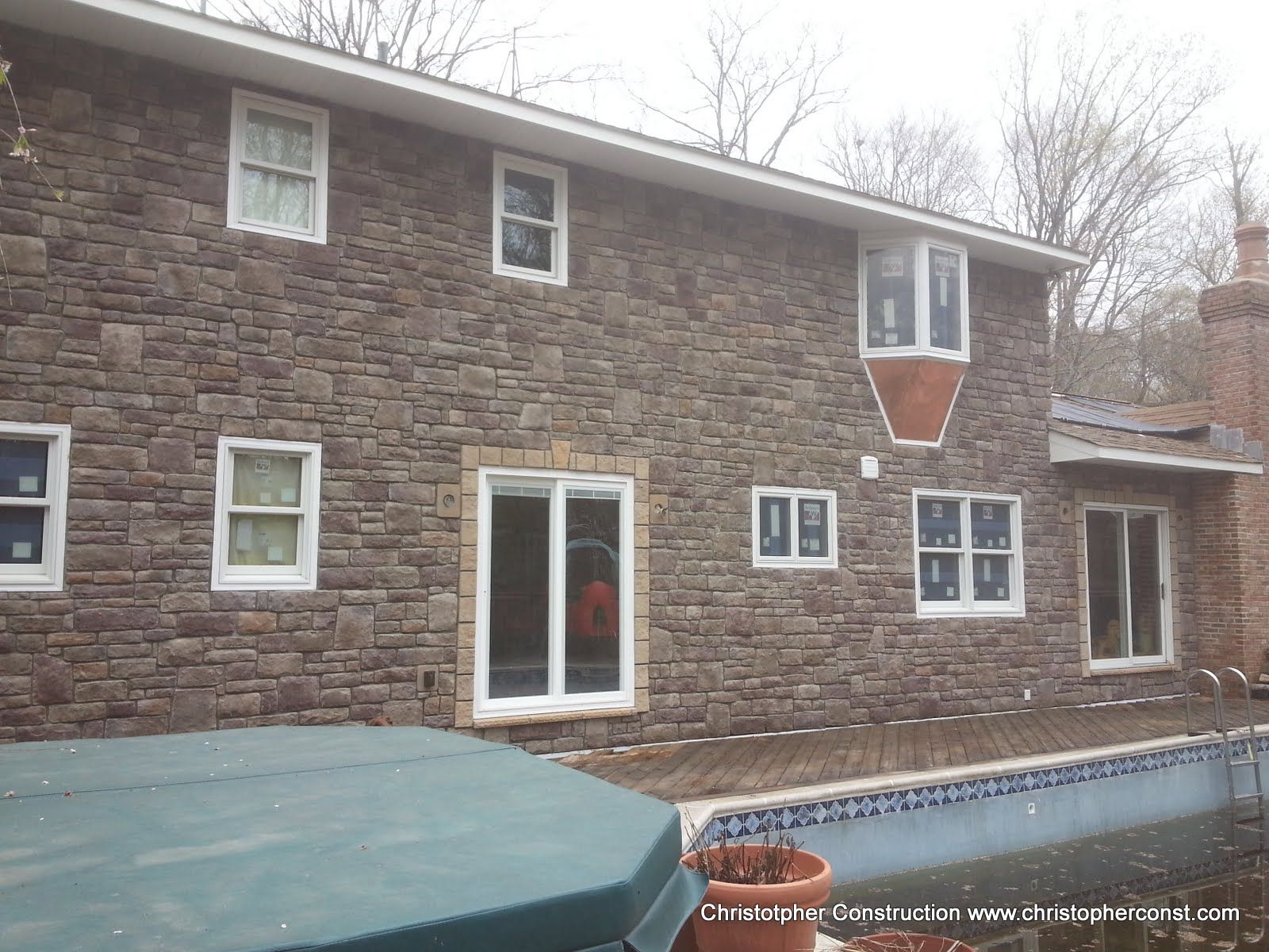 Stone house exterior with white-trimmed windows, a glass door, and a covered pool in the foreground