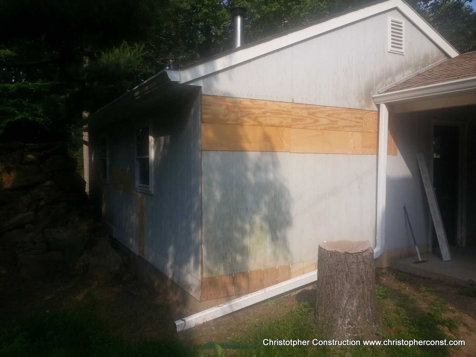 Small white shed with wood trim and sloped roof beside a house in a shaded yard.