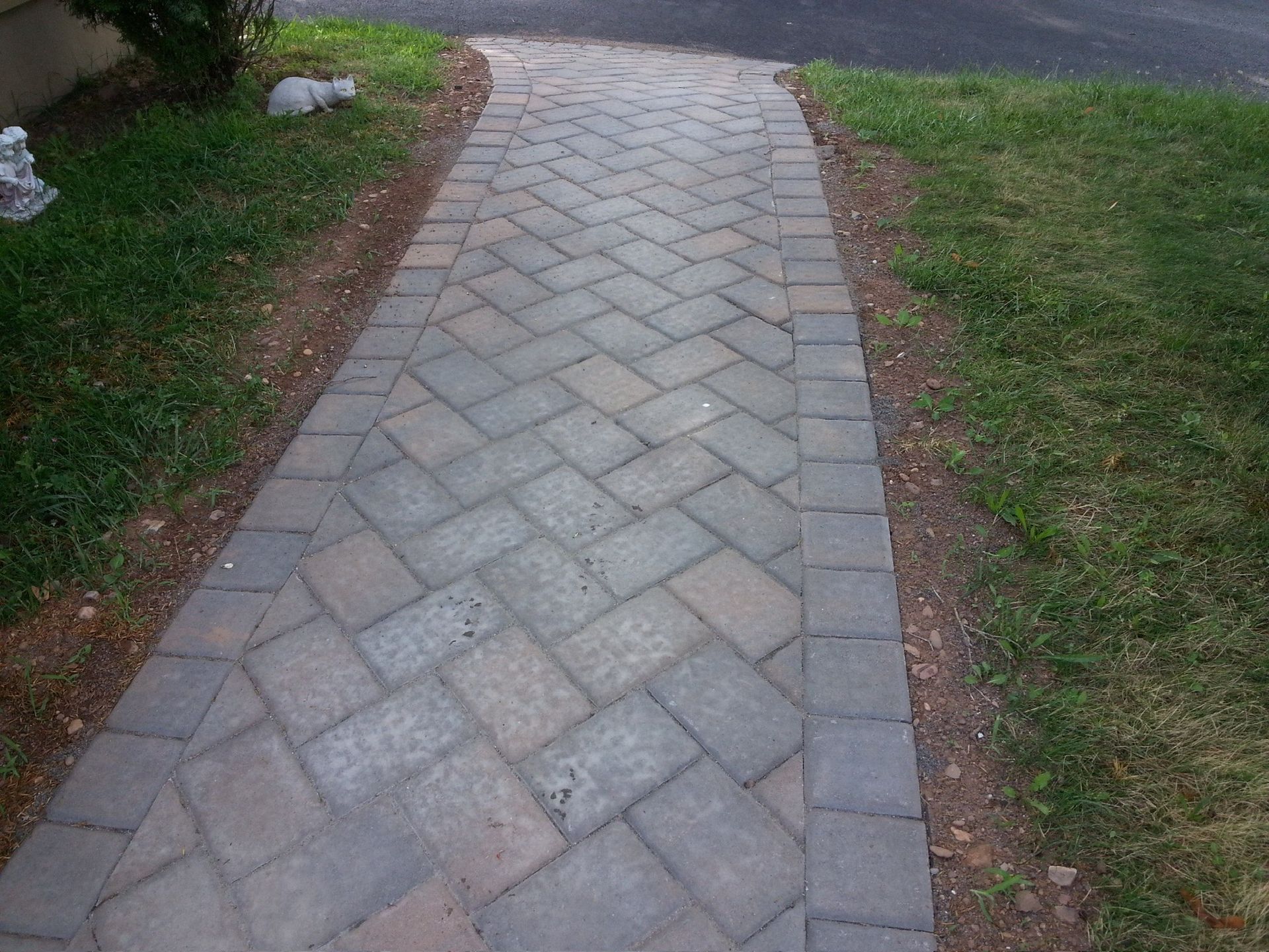 Stone garden walkway bordered by grass and mulch, leading away on a slight curve