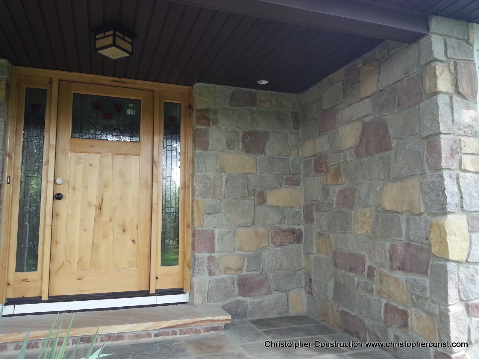 Wooden front door set in a stone porch wall with a small window and overhead light