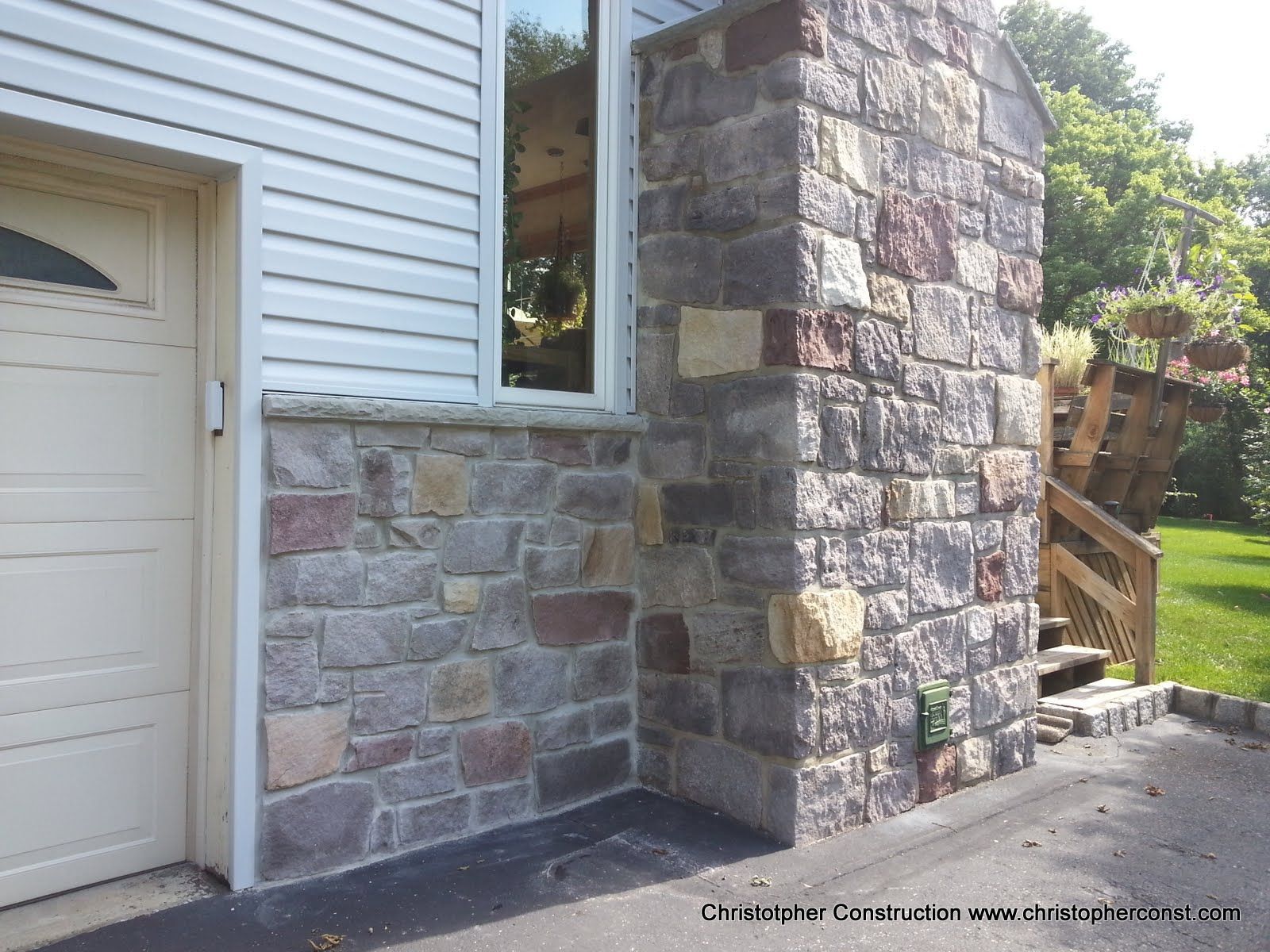 Stone and brick exterior wall with a garage door and a small window beside a wooden deck railing