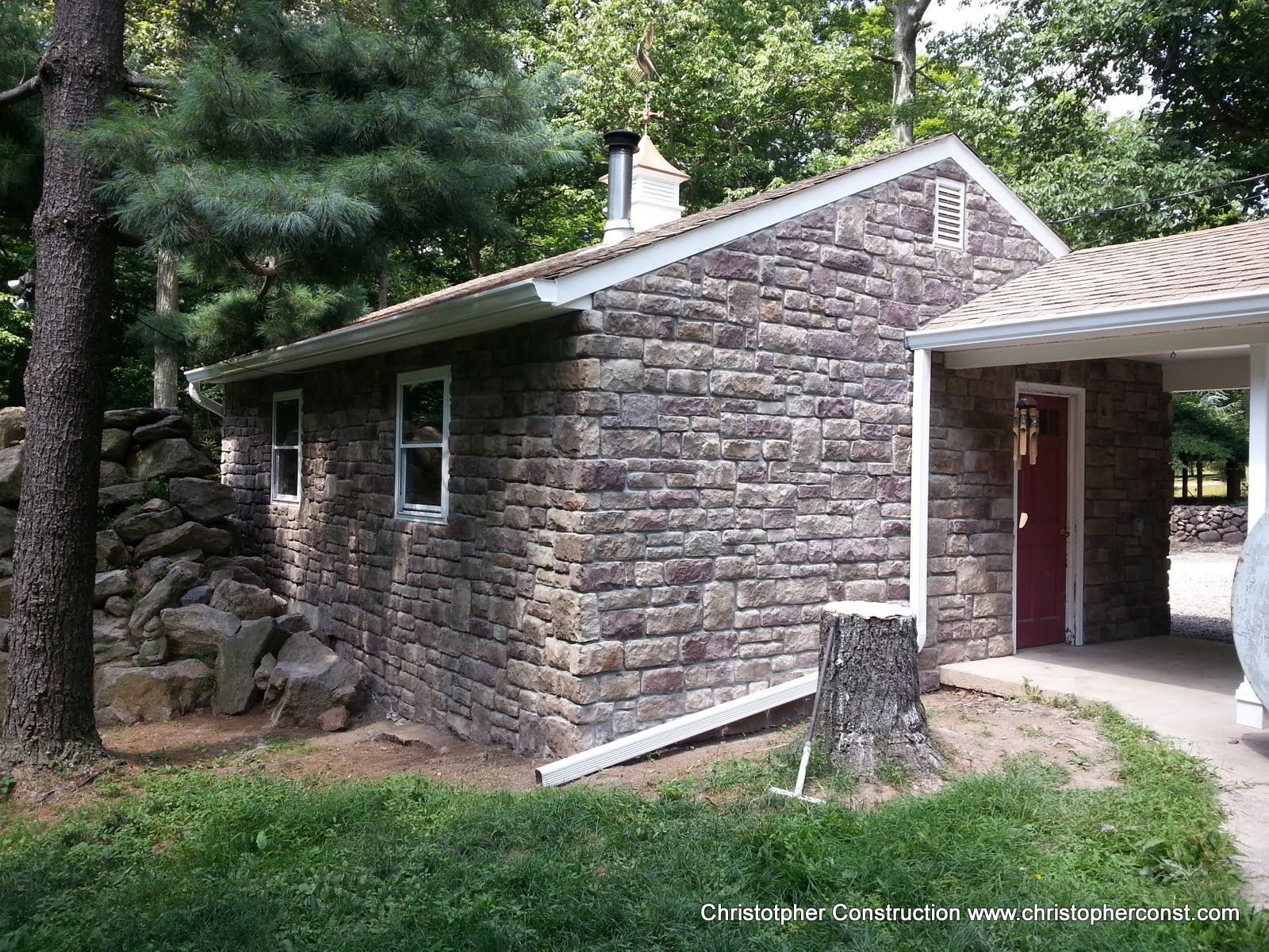 Stone cabin with a red door and carport in a wooded area