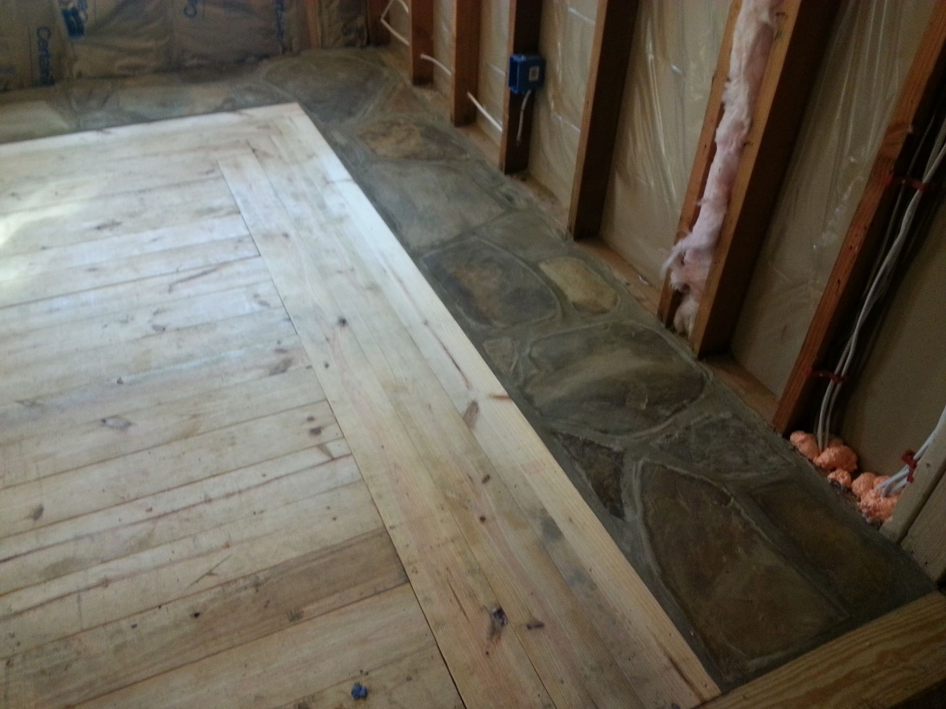 Wooden floor under construction beside a stone border and exposed wall framing