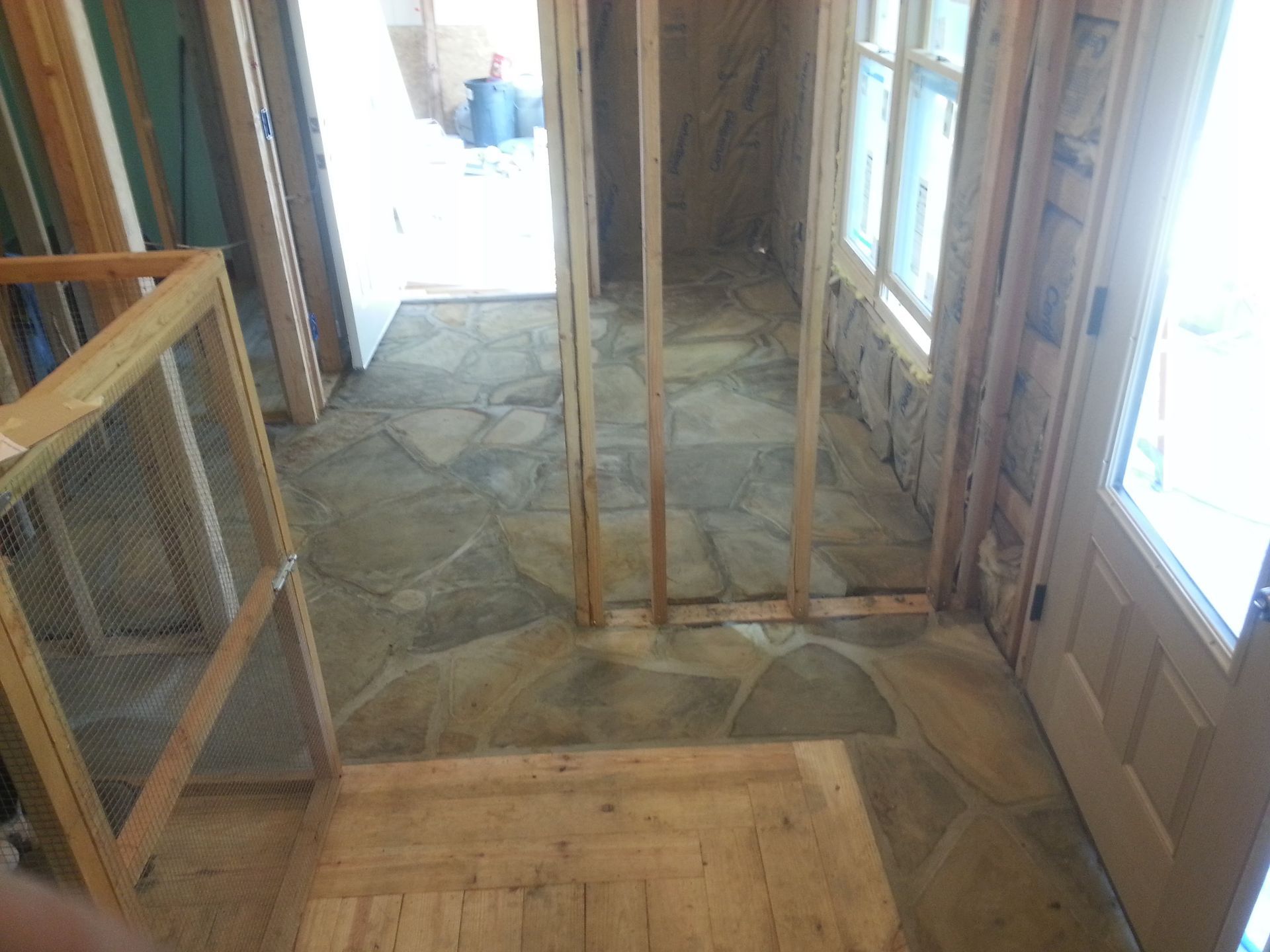 Unfinished hallway with exposed wood framing, stone floor, and doors opening to daylight on both ends