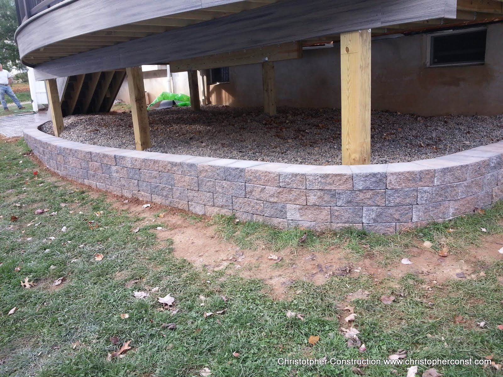 Curved stone foundation supporting a raised wooden structure with yellow posts and a gravel bed underneath