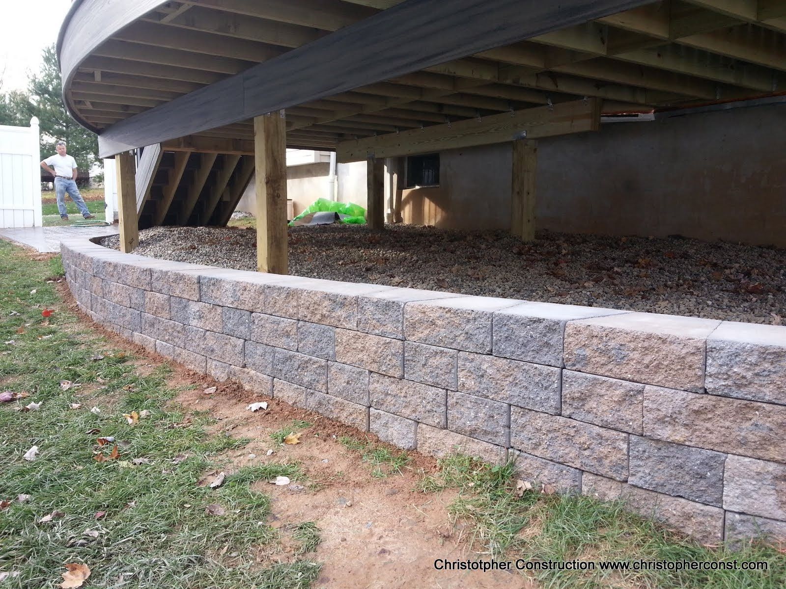 Raised wooden deck with curved stone retaining wall beneath it in a grassy yard