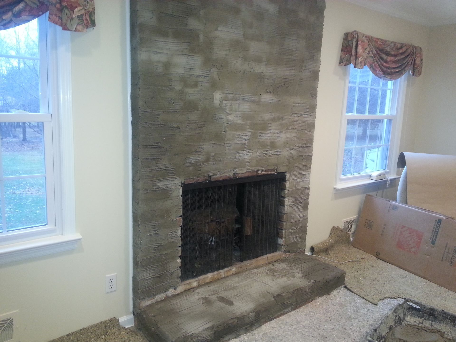 Living room fireplace with stone surround and raised hearth beside two windows and a sofa