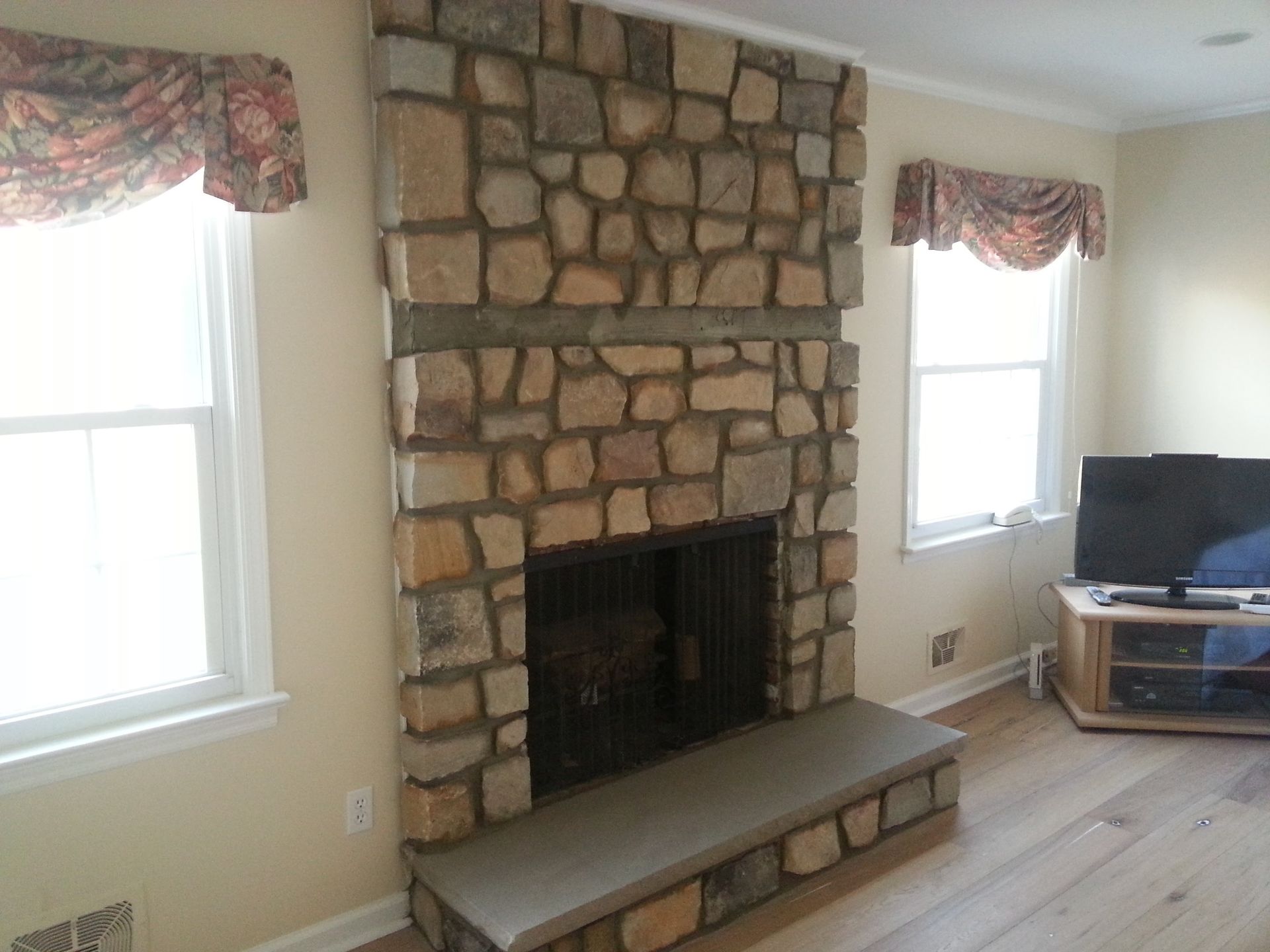 Living room with a stone fireplace, two windows, and a TV on a stand