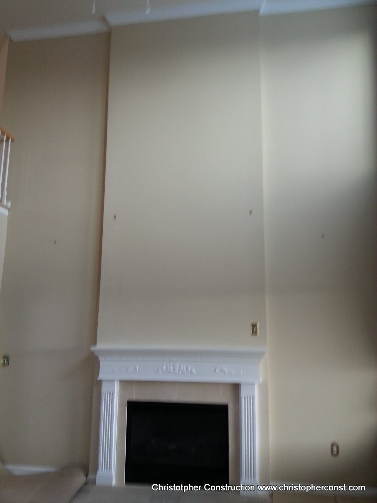 Empty beige living room wall with a white fireplace mantel and ceiling vents.