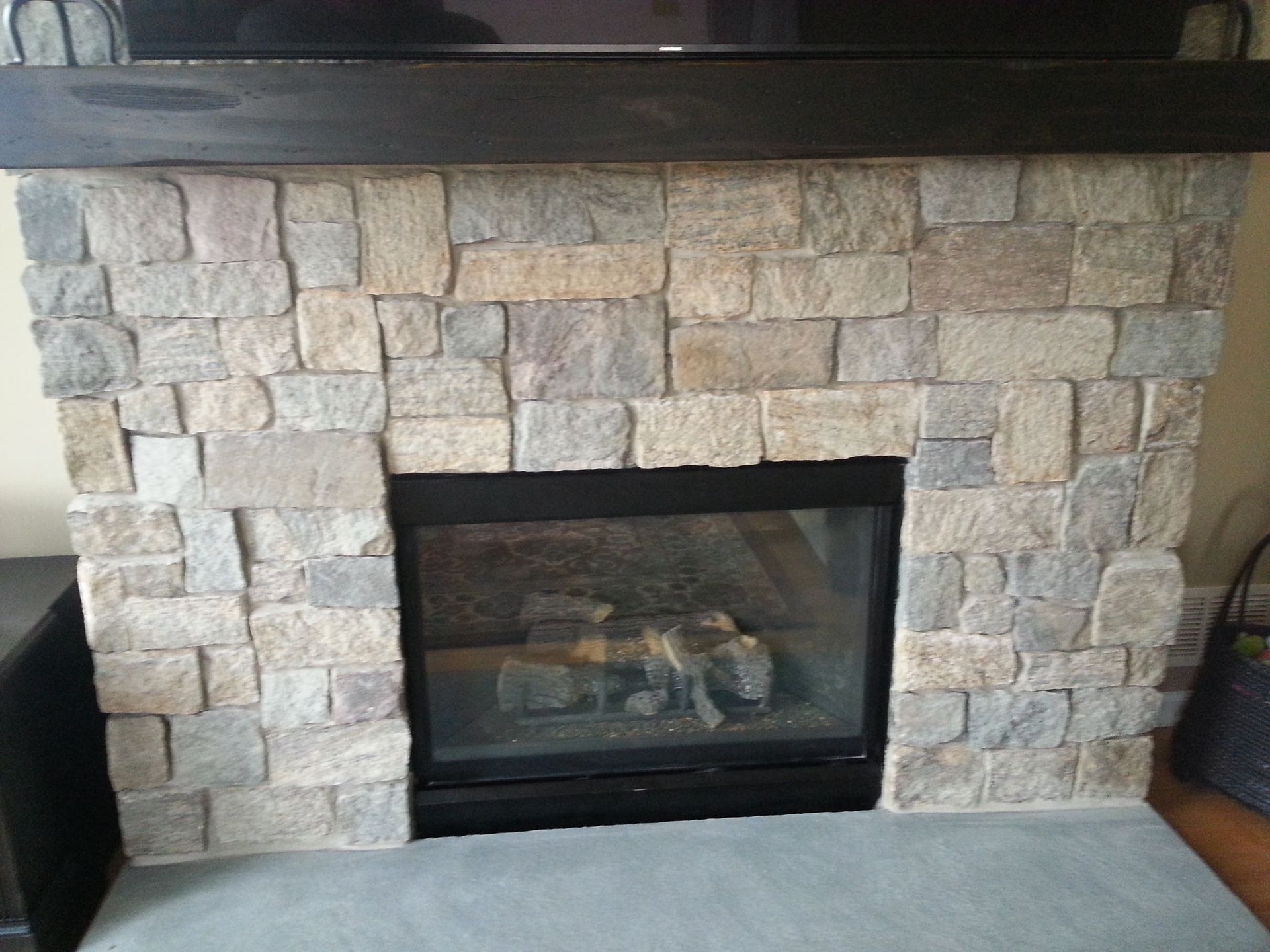Stone fireplace with black glass insert in a living room, framed by dark mantle and side walls