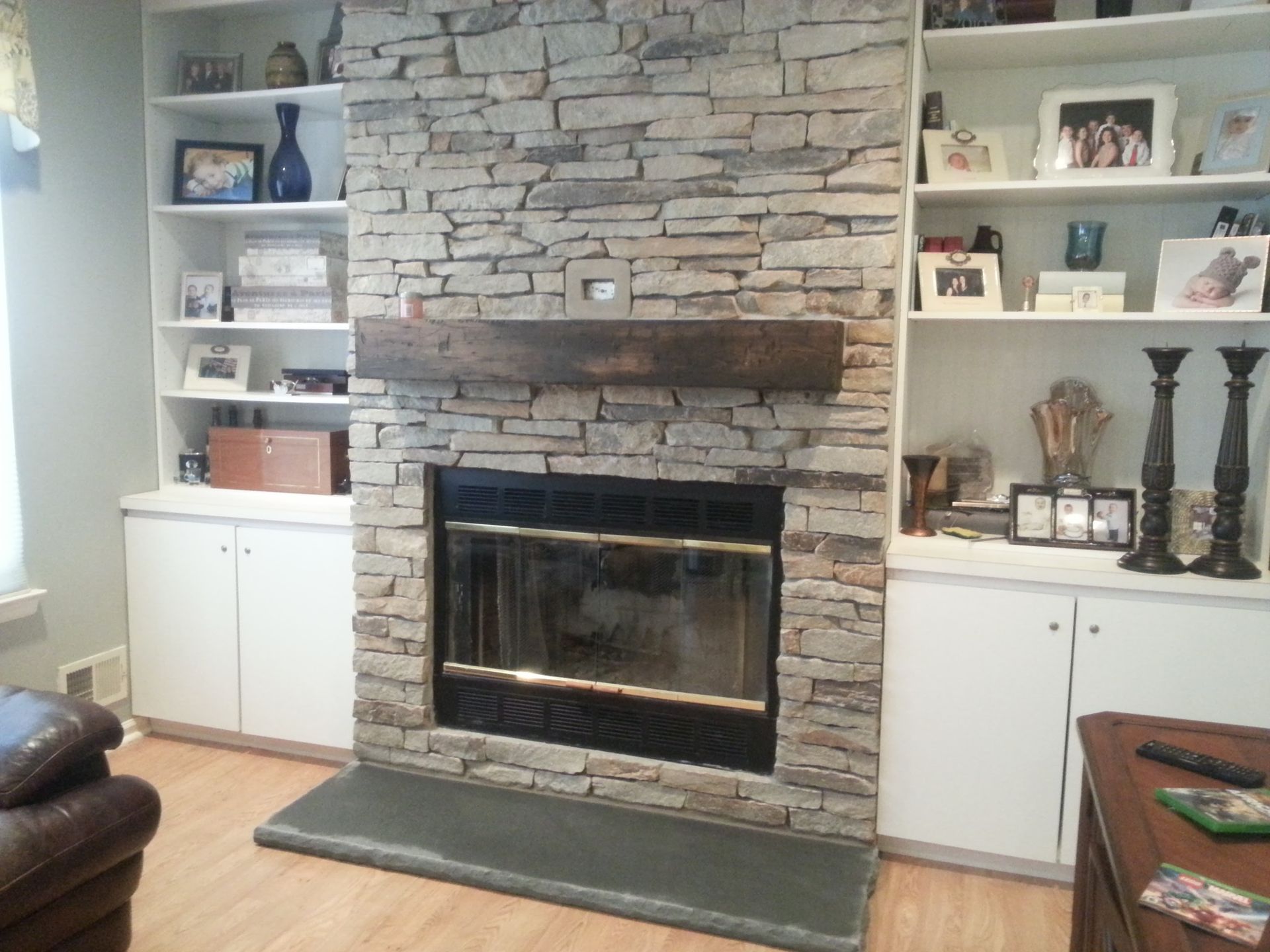 Living room fireplace with stone surround, built-in shelves, and white cabinets