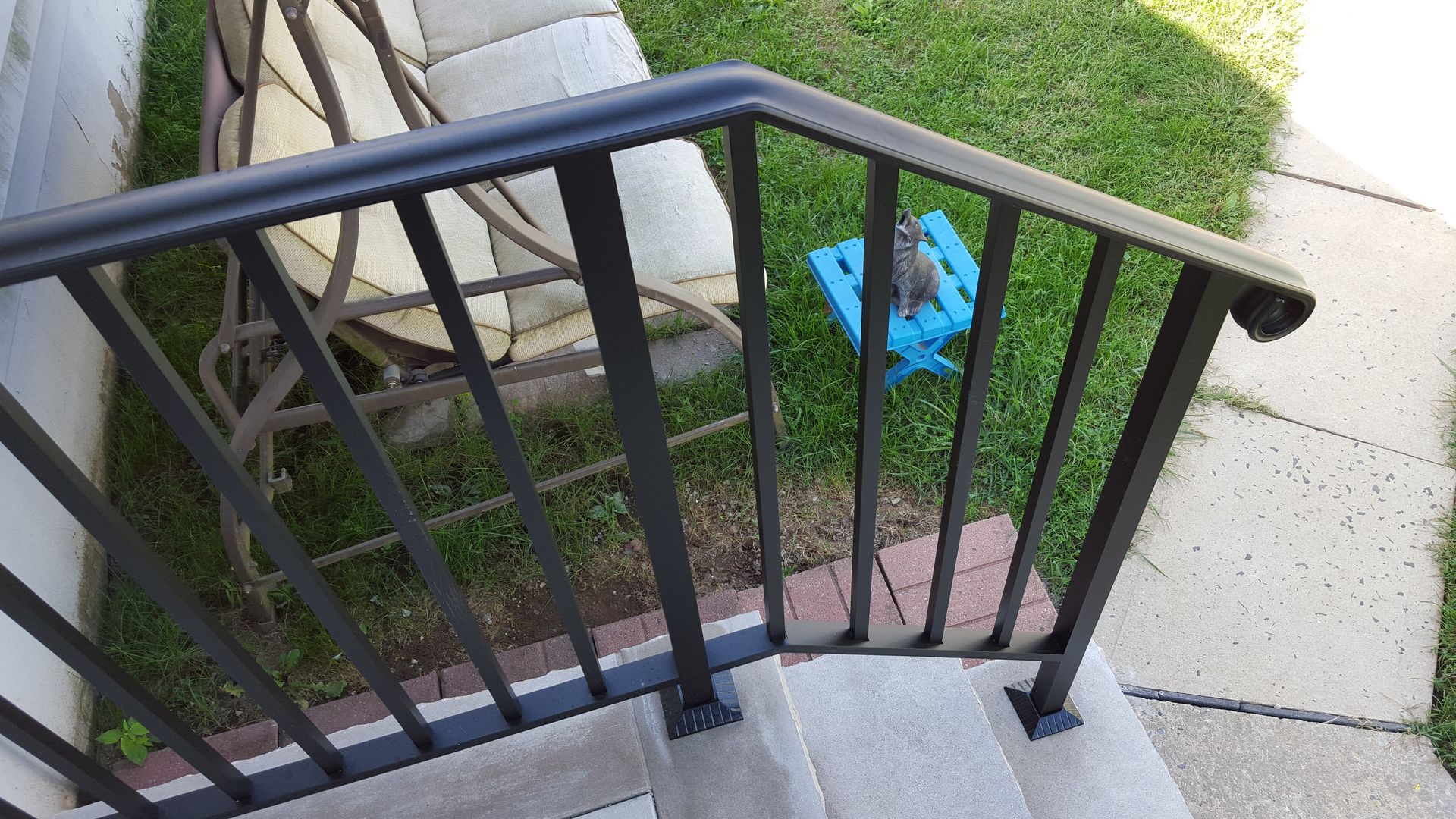 Black metal stair railing beside concrete steps, overlooking a yard with a blue object on the grass.