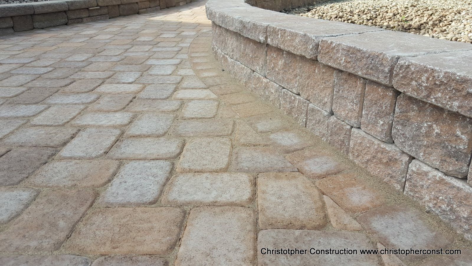 Stone-paver walkway beside a raised retaining wall in a landscaped outdoor area.