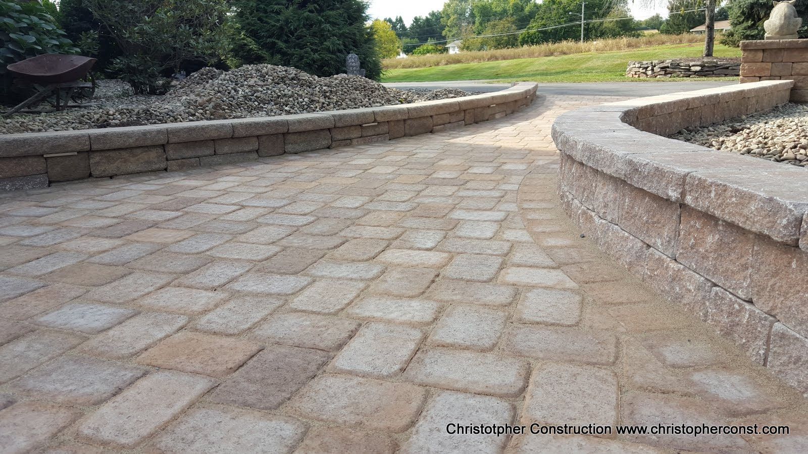 Curved stone-paved walkway beside a low wall in a landscaped outdoor park area