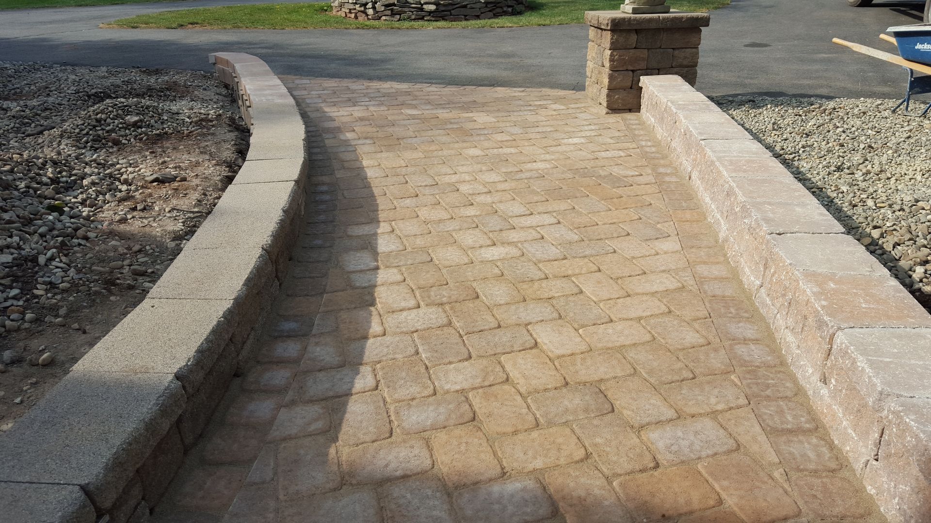 Curved tan brick walkway beside a gravel garden and stone border wall outdoors