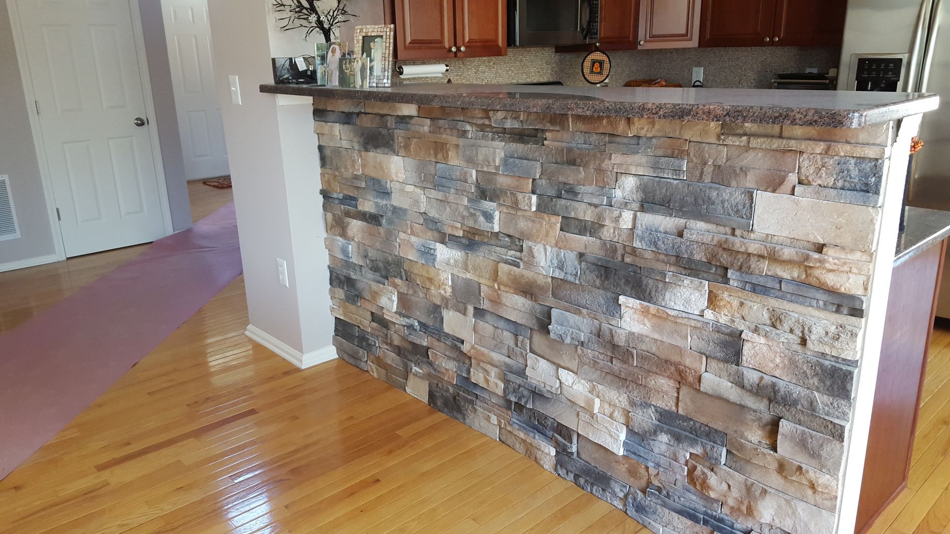 Stone-faced kitchen island with granite countertop in a hardwood-floored home interior