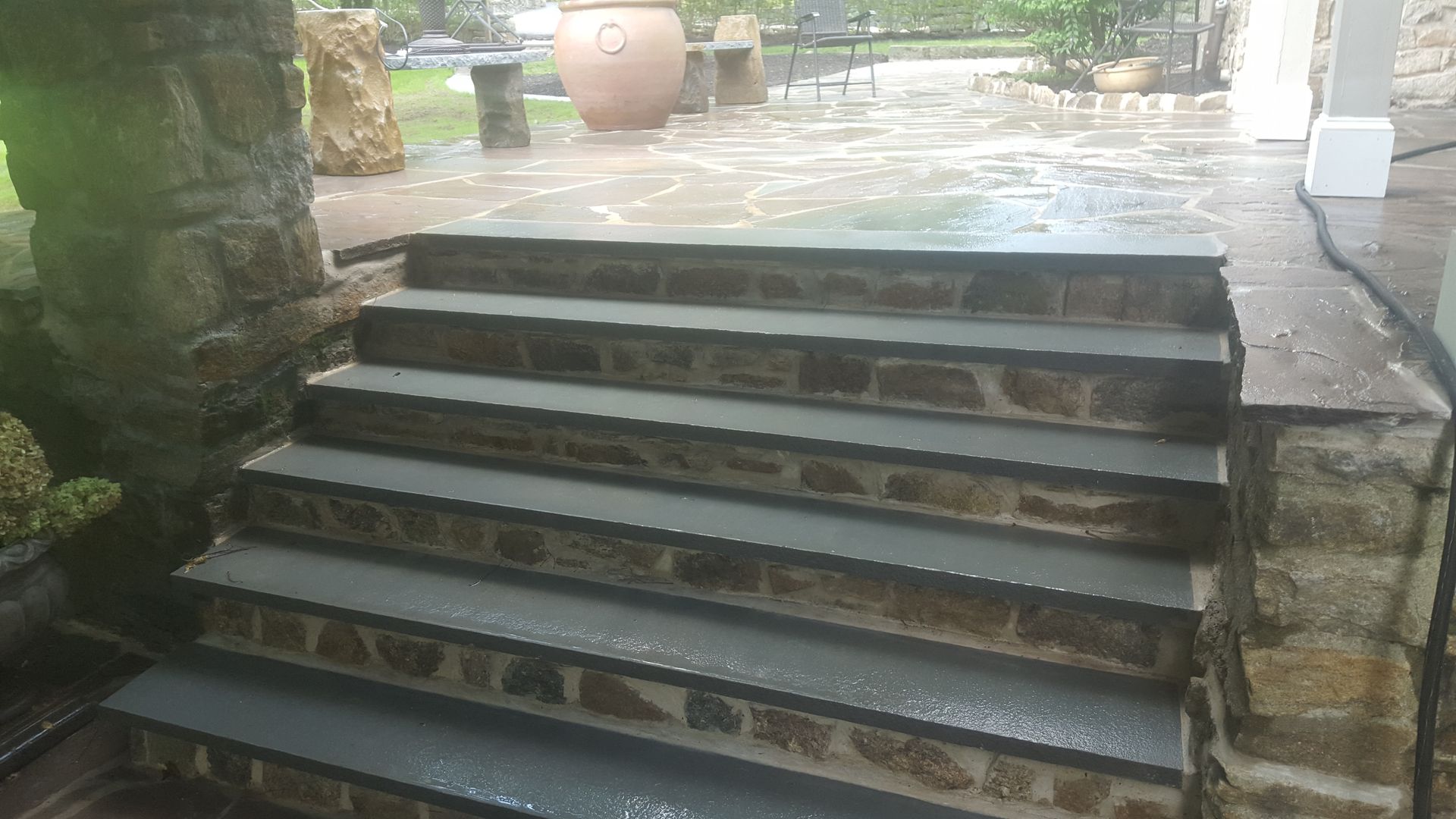 Stone outdoor steps leading to a patio, with a large urn and greenery in the background.