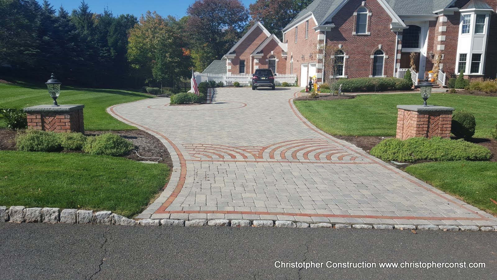 Curved stone driveway leading to brick houses with manicured lawns and flower beds