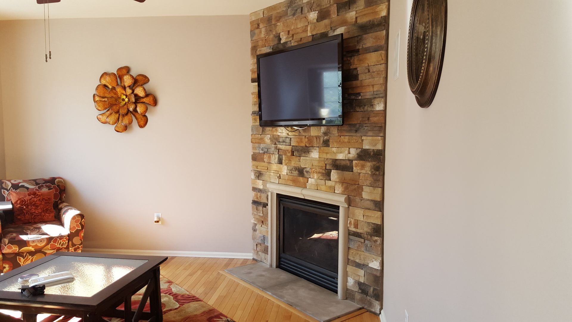 Living room with stone fireplace, wall-mounted TV, orange decor, and patterned armchair
