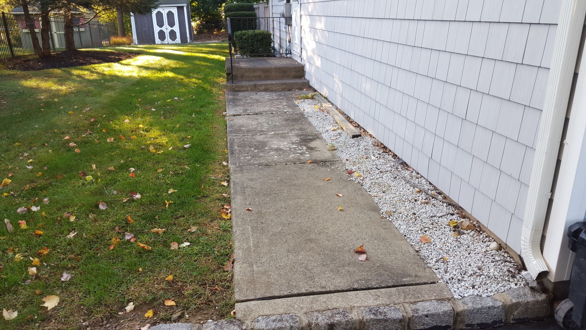 Narrow concrete side path beside a house, with grass on one side and white gravel along the wall.