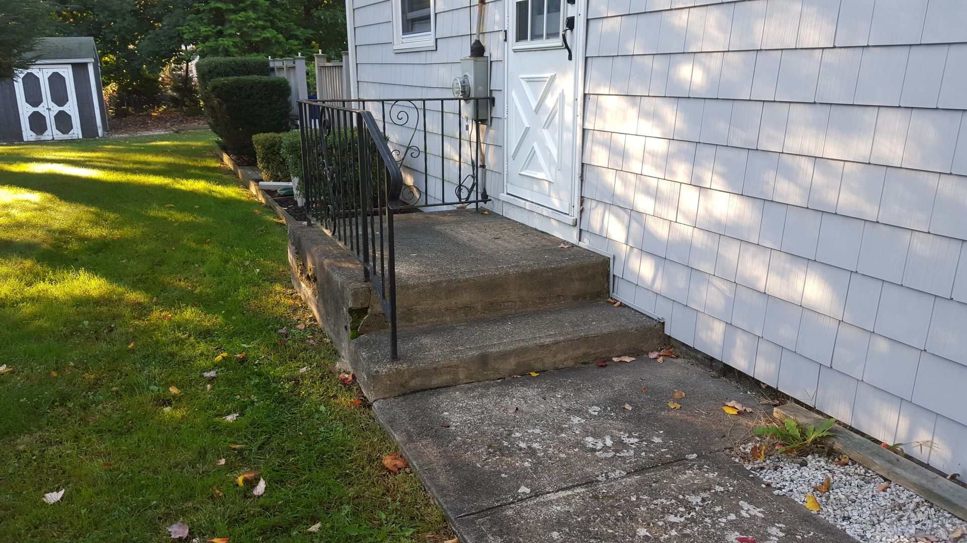 Front steps and white house siding beside a small lawn with a target board in the yard