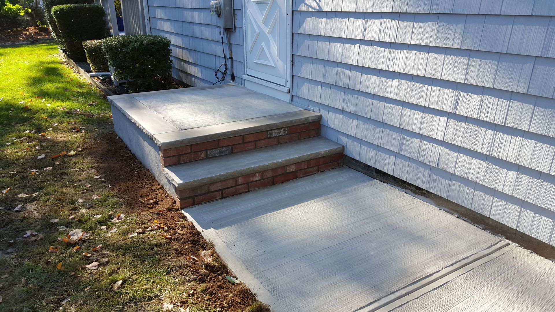 Concrete front steps and walkway beside a white house with blue siding and a small hedge