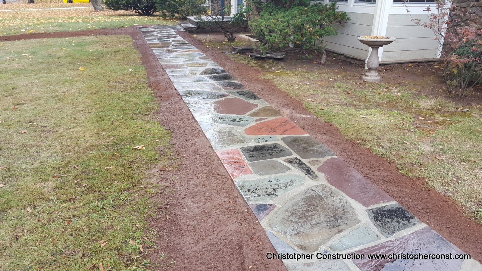 Stone walkway bordered by red brick and grass leading to a white house entrance