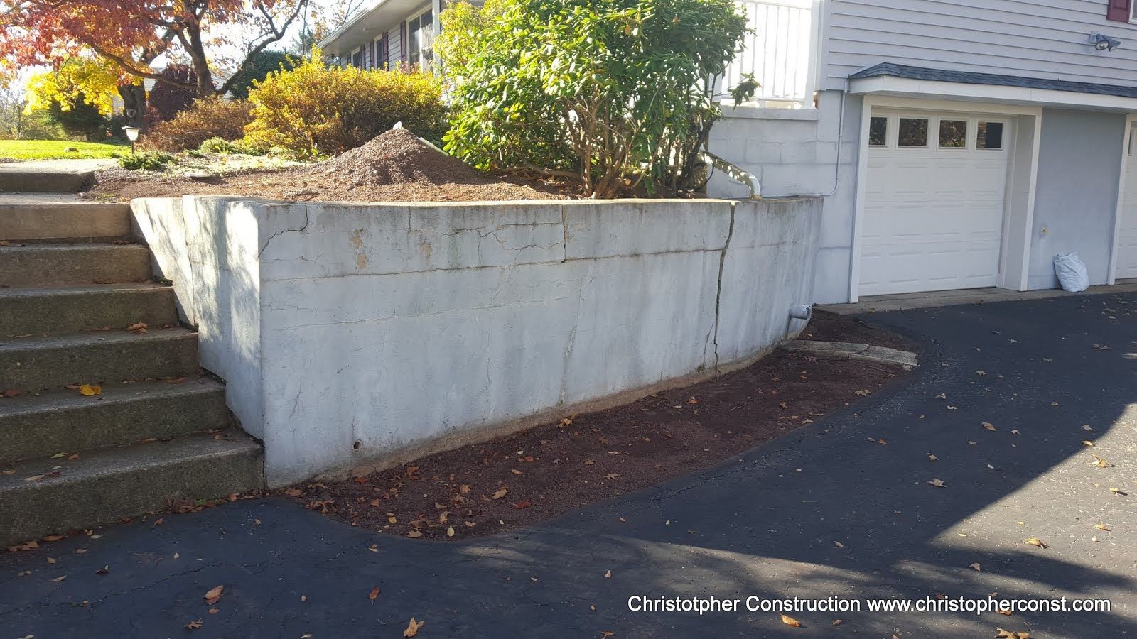 Driveway beside concrete retaining wall and steps leading to a garage, with autumn leaves scattered below
