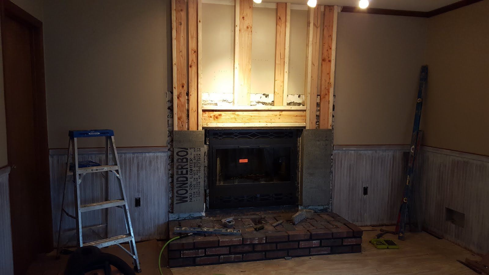 Room with a fireplace, ladder on the left, and unfinished wall paneling in a dim interior.