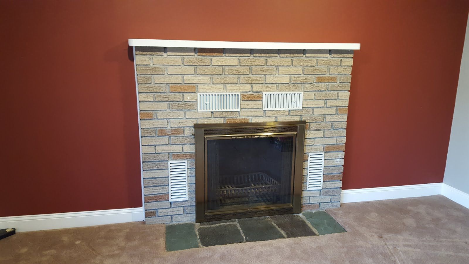 Brick fireplace with black firebox in a room with red walls and beige carpet