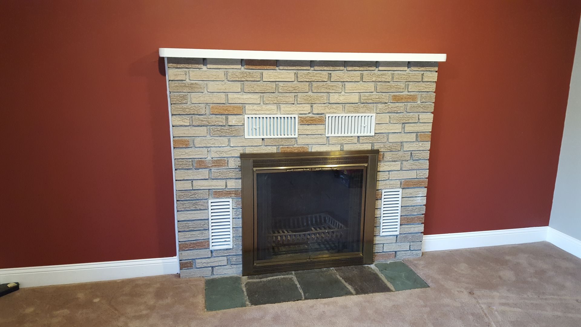 Brick fireplace with white mantel and black firebox against a red wall in a living room