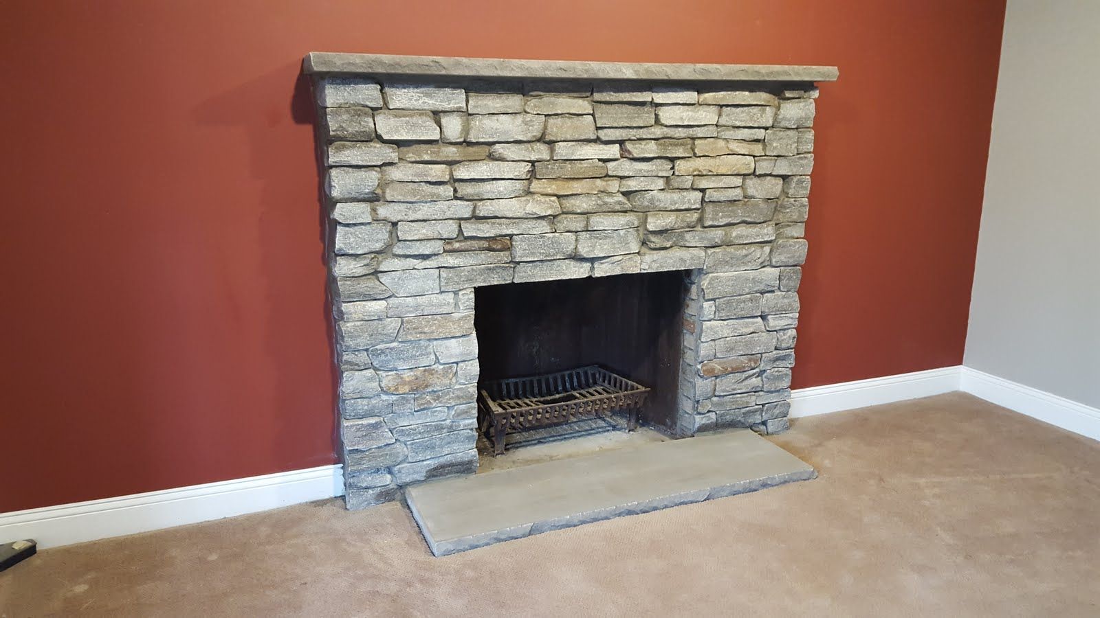 Stone fireplace with black firebox against a red wall in an empty room