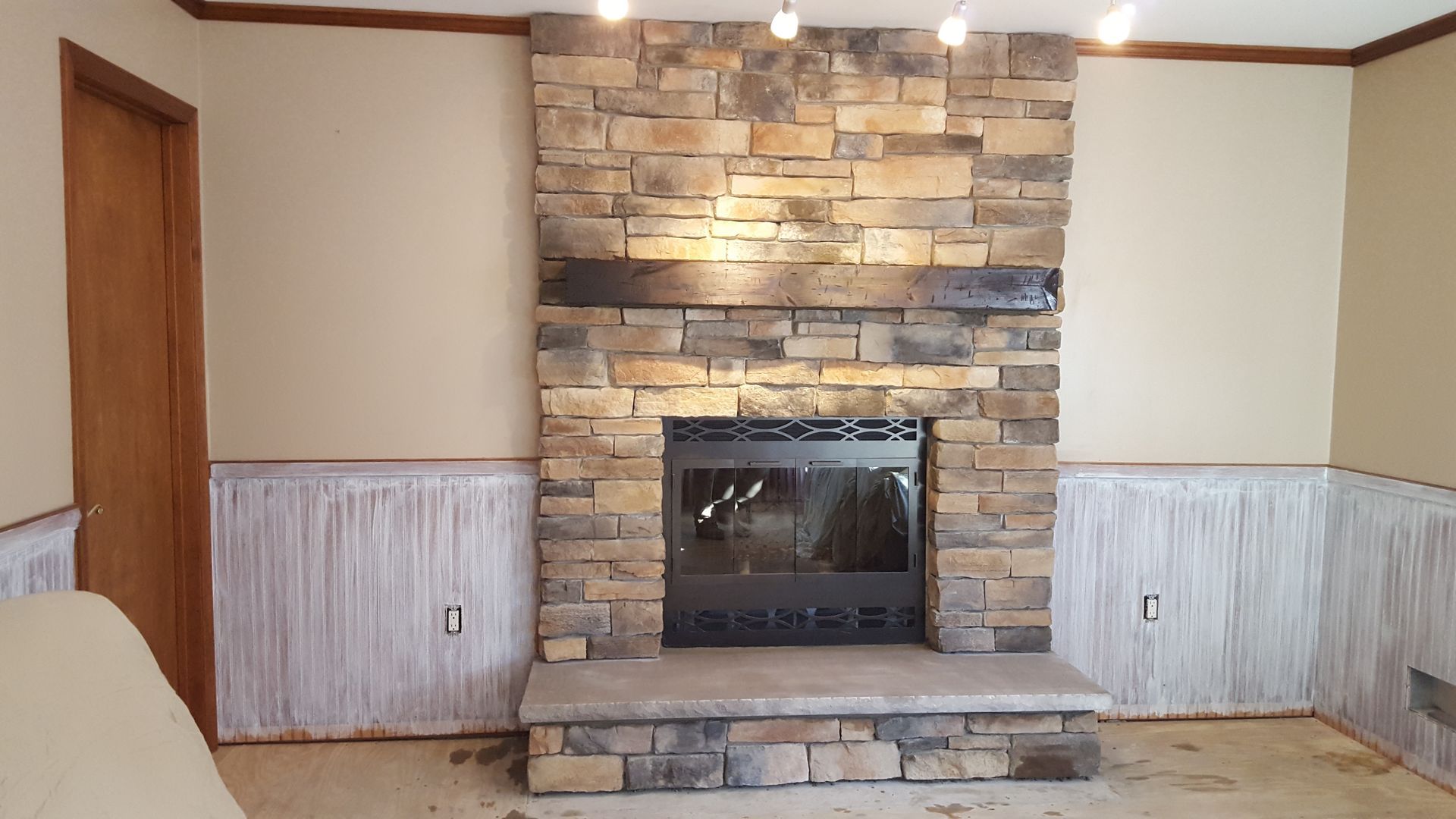 Living room fireplace with stacked stone surround, white wainscoting, and a beige carpeted hearth.