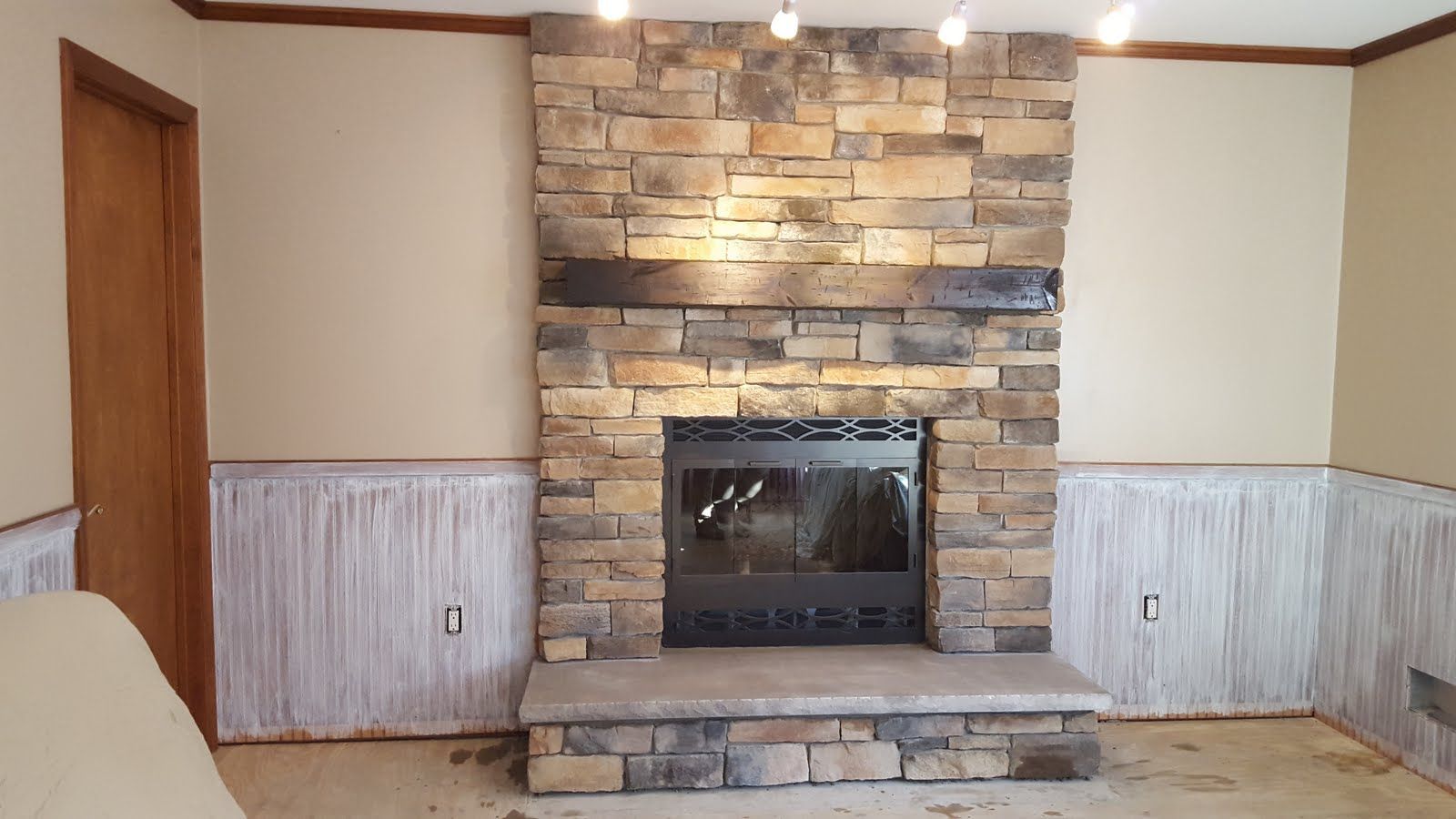 Living room with stone fireplace, white wainscoting, wood trim, and beige walls