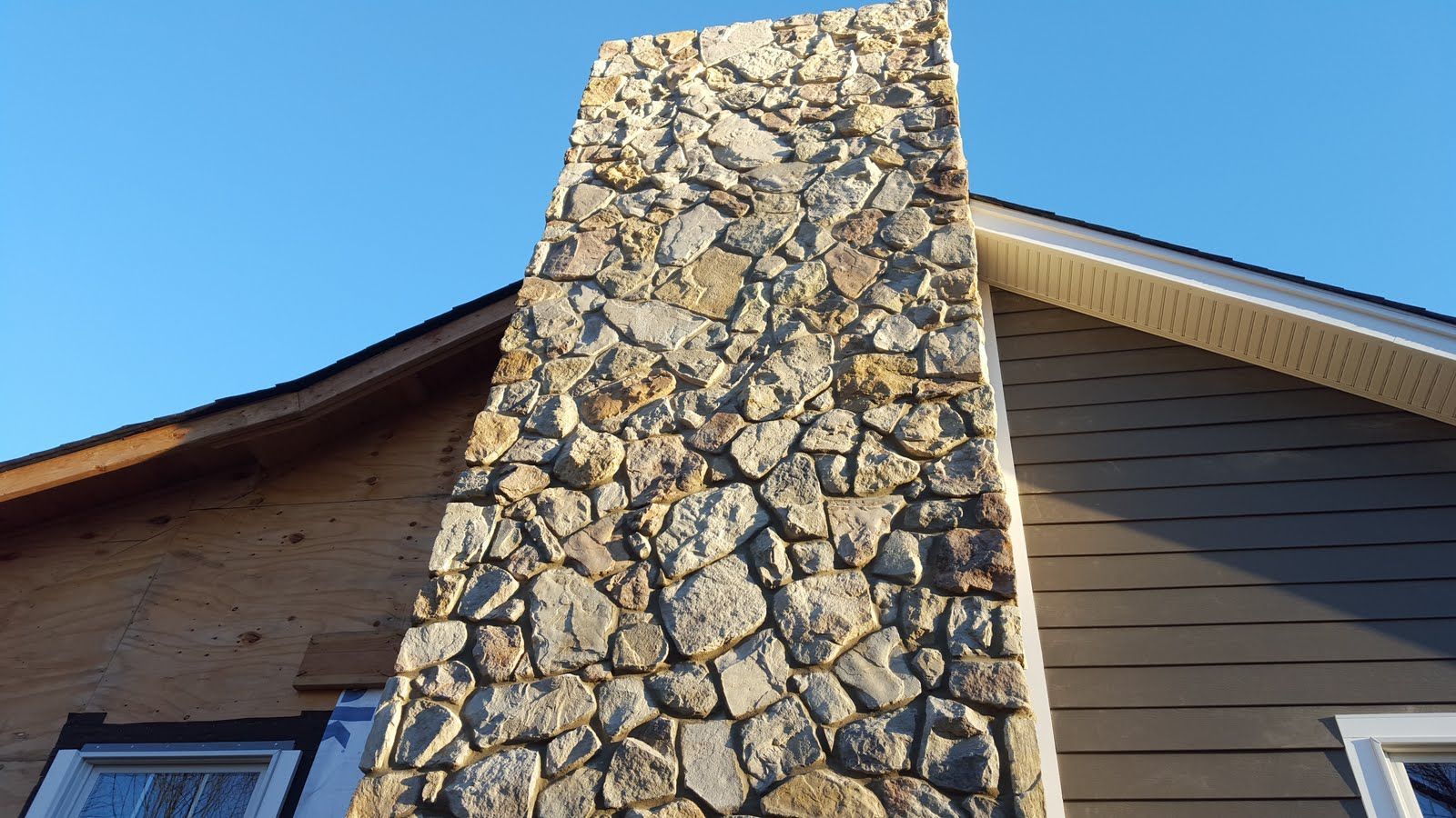 Stone chimney rising beside a tan house roof against a blue sky