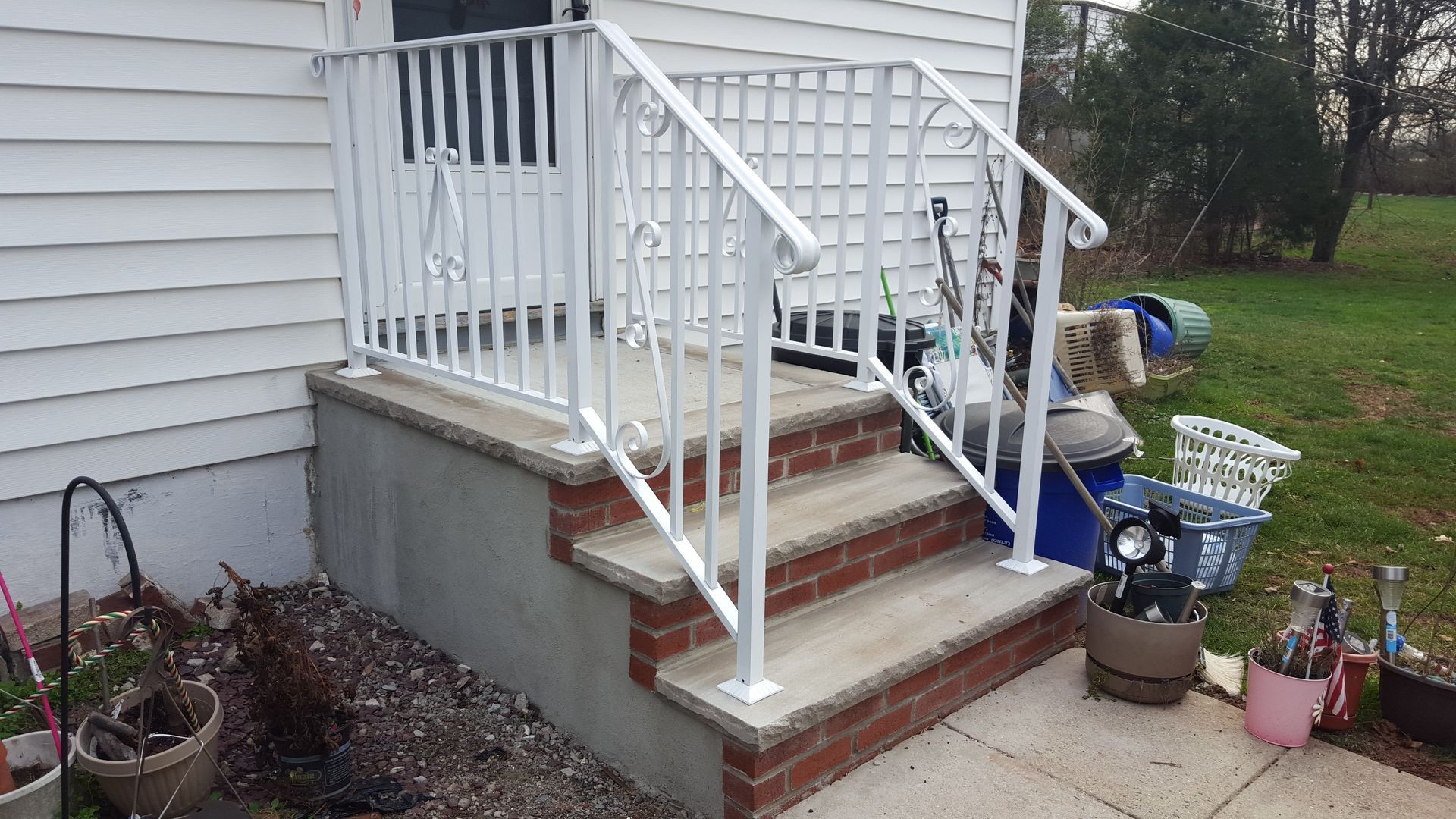 Front porch steps with white railing, red brick, and small potted items beside a house