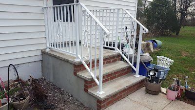 Front porch steps with white railing and brick risers on a house exterior.
