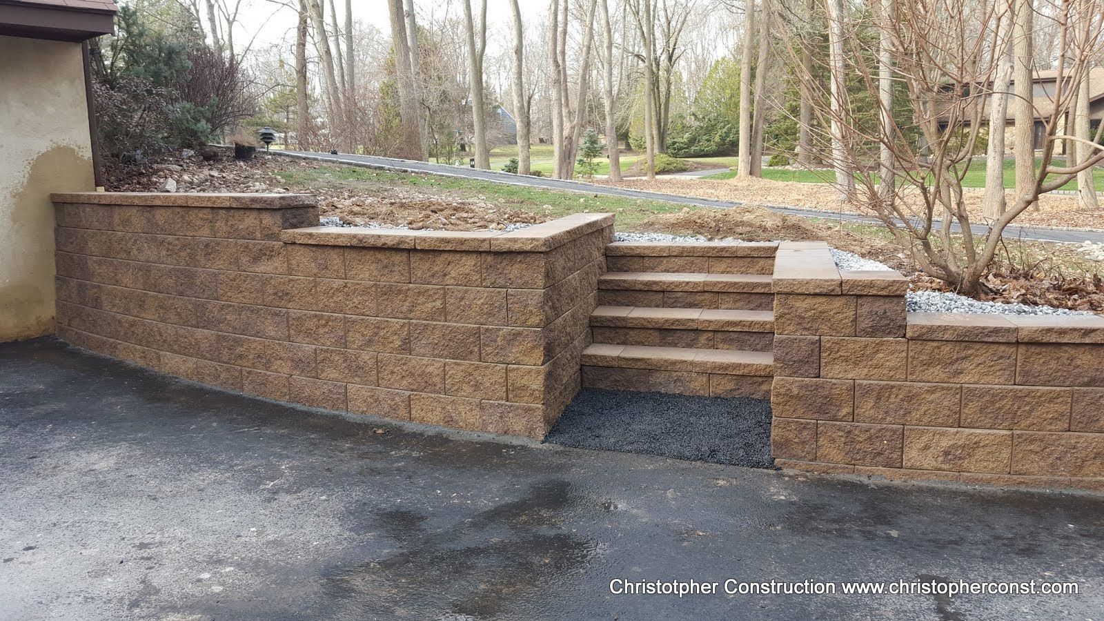 Backyard stone retaining wall with steps leading to a gravel path and wooded garden area
